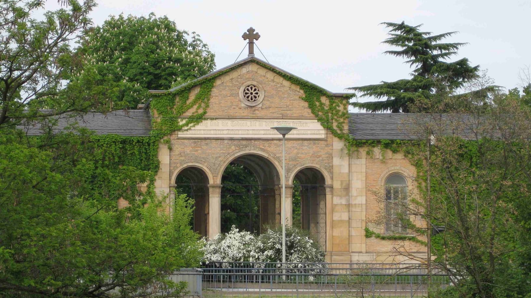 Efeubewachsener Backsteineingang mit drei Rundbögen, Rosettenfenster und Kreuz auf Hauptfriedhof Mannheim